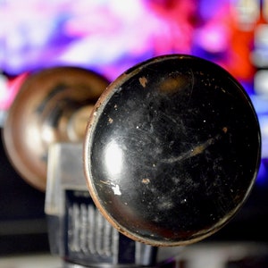 May include: A vintage car horn with a black metal bell and a brass base. The horn is in focus, while the background is blurred.