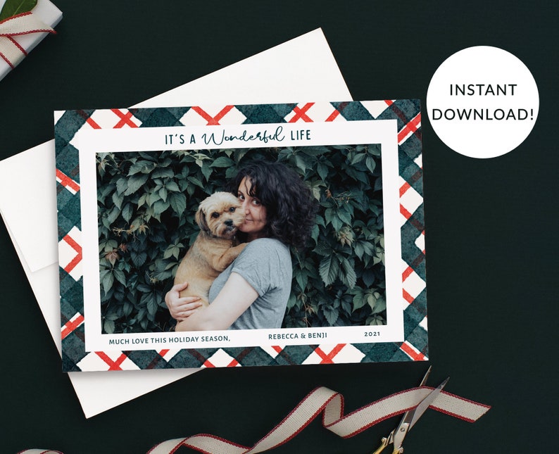 May include: A Christmas card with a green and red plaid border. A photo of a woman holding a dog in front of a green bush is in the center. The text "It's a Wonderful Life" is at the top of the card. The text "Much love this holiday season, Rebecca & Benji 2021" is at the bottom of the card.