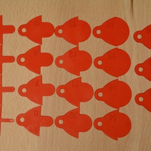 May include: Twenty red plastic tags with numbers 1 through 20 printed on them. The tags are shaped like teardrops with a small hole at the top.