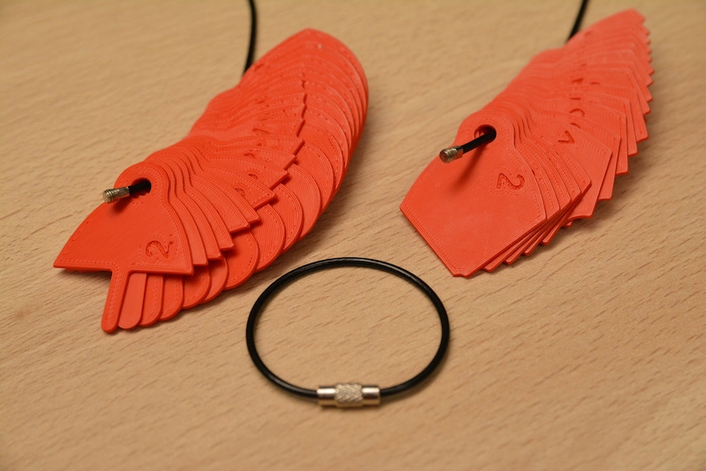 May include: Two sets of red plastic numbered tags on black cords. The tags are in the shape of a crescent moon and are numbered 1 through 12. A black cord with a silver clasp is also pictured.