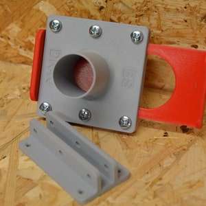 May include: A grey plastic component with a cylindrical opening and a red attachment. The component is secured with screws and includes the text "DIVU" and "BS". A separate grey bracket is also present. The items are on a wood surface.