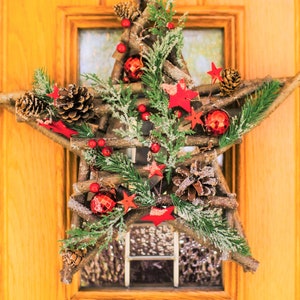 May include: A rustic star-shaped Christmas wreath made of twigs, decorated with pine cones, red berries, and red stars. The wreath is hanging on a wooden door.