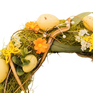 K&ouml;nnte beinhalten: Ein gr&uuml;ner und brauner Osterkranz, der mit gelben und orangefarbenen Blumen, gelben Schmetterlingen und gelben Eiern verziert ist.