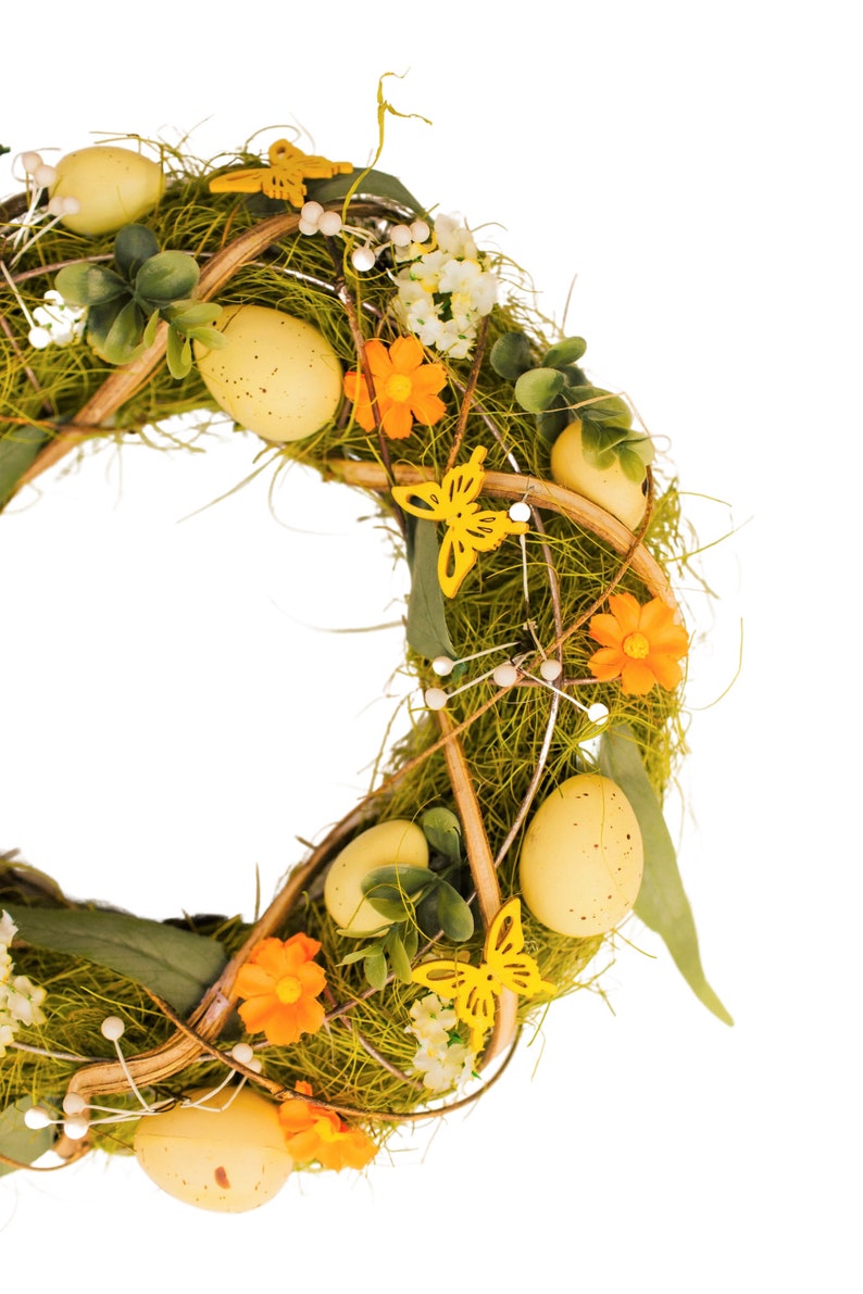K&ouml;nnte beinhalten: Ein gr&uuml;ner Osterkranz mit gelben Eiern, Schmetterlingen und orangefarbenen Blumen.