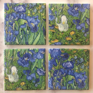 May include: Set of four square ceramic coasters featuring a vibrant, impressionistic painting of blue irises and white flowers against a green background.