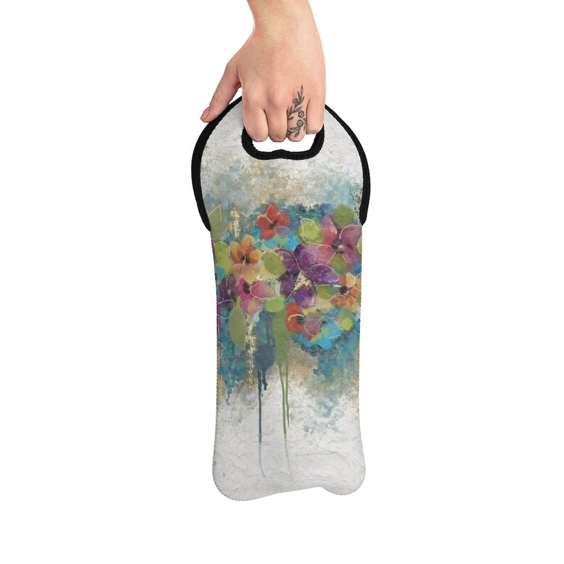 Op de afbeelding: Een zwart-witte wijnfles draagtas met een kleurrijk bloemenontwerp. De draagtas heeft een zwarte handvat en een witte achtergrond met een aquarel-bloemenpatroon.