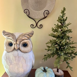 May include: A white wooden owl figurine with large eyes, a blue speckled ceramic pumpkin, and a small green felt Christmas tree on a wooden surface.