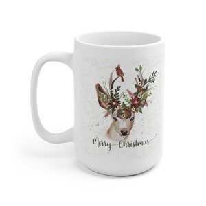 May include: White ceramic mug with a deer illustration. The deer has a floral crown with red flowers and green leaves. A cardinal bird is perched on one of the antlers. The text "Merry Christmas" is printed below the deer.