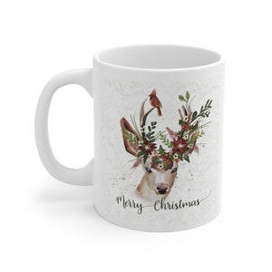 May include: White ceramic mug with a watercolor illustration of a deer with a floral crown and a cardinal perched on its antlers. The text "Merry Christmas" is written below the deer.