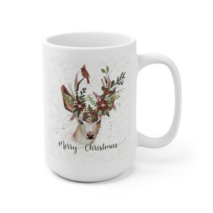 May include: White ceramic mug with a watercolor illustration of a deer with a floral crown and a cardinal perched on its antlers. The text "Merry Christmas" is written in cursive below the deer.