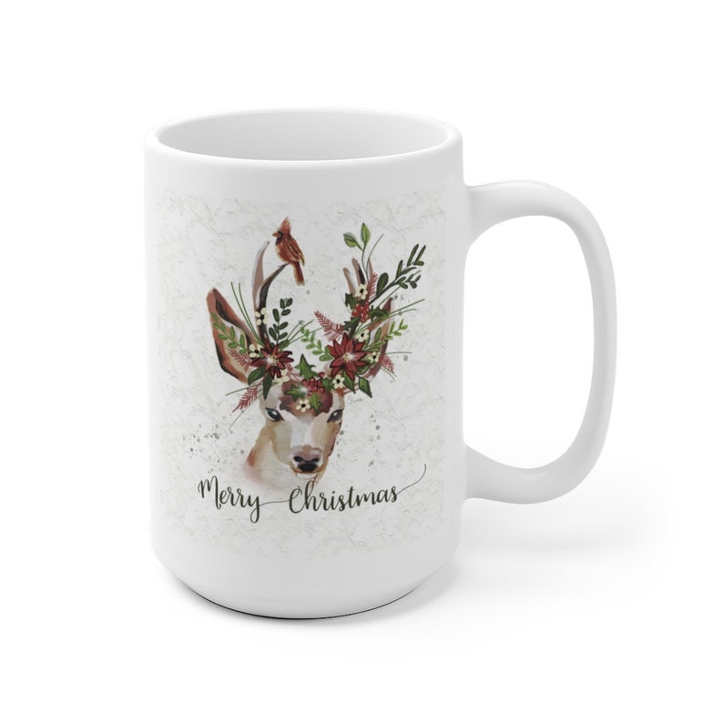 May include: White ceramic mug with a watercolor illustration of a deer with a floral crown and a cardinal perched on its antlers. The text "Merry Christmas" is written in cursive below the deer.