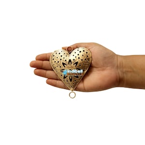 A hand displaying a heart-shaped metal cutout with rustic vintage detailing and a floral pattern.