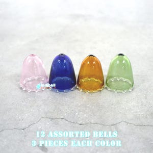 May include: Four glass bells in pink, blue, orange, and green colors. Each bell has a scalloped edge. The text below the bells reads: '12 ASSORTED BELLS 3 PIECES EACH COLOR'