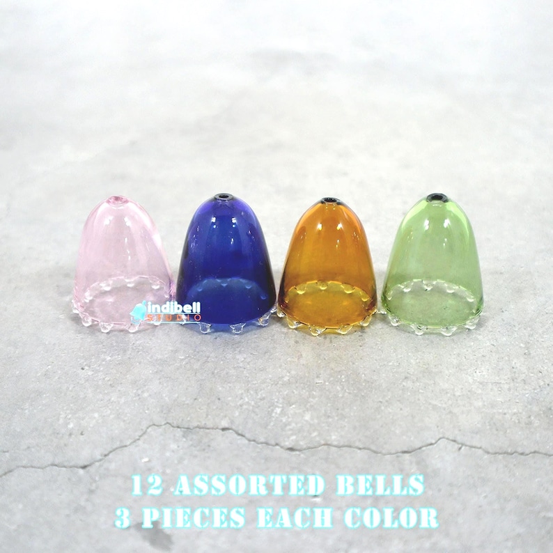 May include: Four glass bells in pink, blue, orange, and green colors. Each bell has a scalloped edge. The text below the bells reads: '12 ASSORTED BELLS 3 PIECES EACH COLOR'
