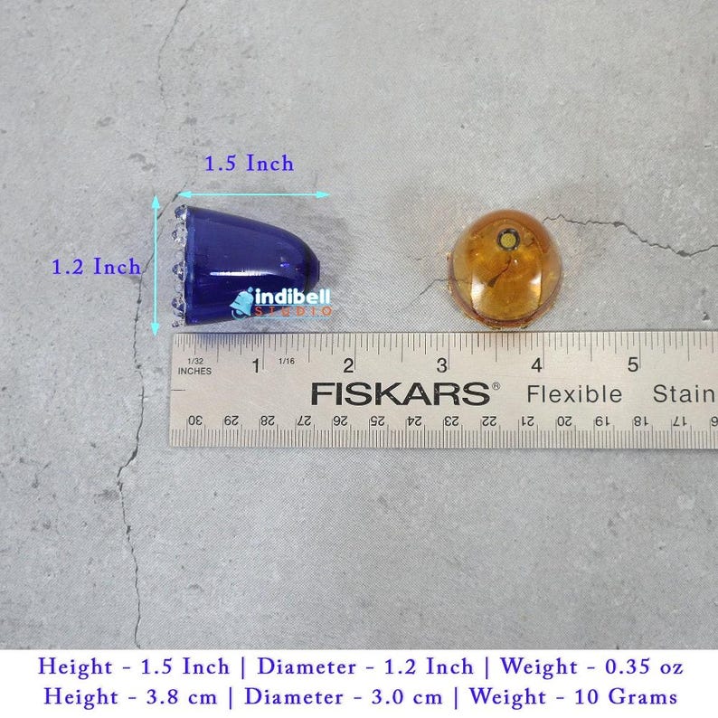 K&ouml;nnte beinhalten: Ein blaues, kegelf&ouml;rmiges Objekt und ein rundes, bernsteinfarbenes Objekt &uuml;ber einem Fiskars-Lineal. Das blaue Objekt ist 3,8 cm lang und hat einen Durchmesser von 3,0 cm. Der Text indibell studio ist in der N&auml;he des blauen Objekts sichtbar.