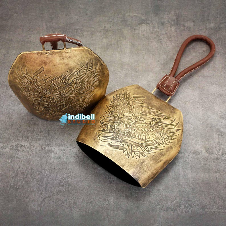 The large cow bells with American bald eagle design and american flag engraved on it shown on a granite backdrop.