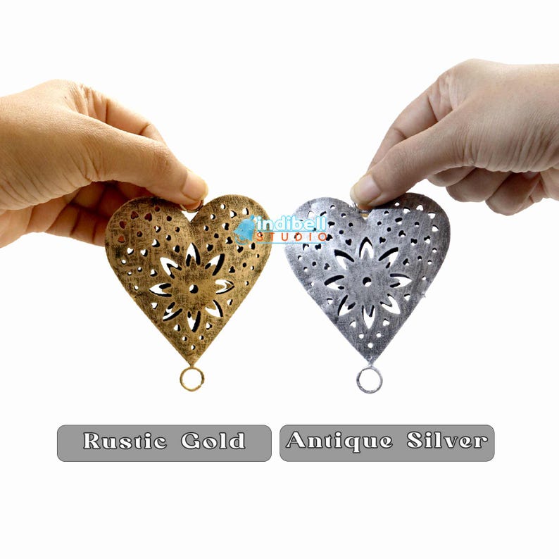 the rustic gold and antique silver heart shape blanks held in hand showing their detailed engraving and the textures of the heart.