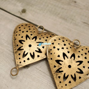 Close up view of two rustic heart shaped metal cutouts with detailed floral patterns, lying on a wooden surface.