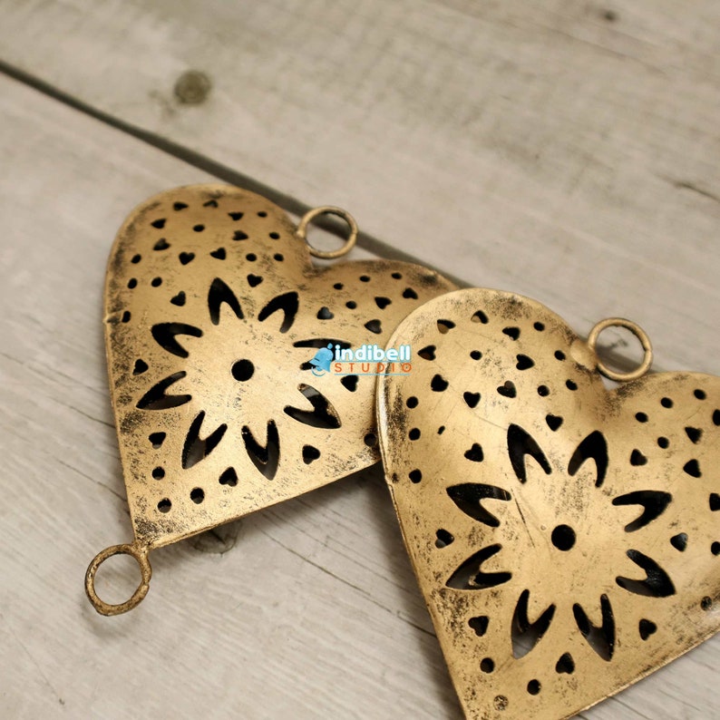 Close up view of two rustic heart shaped metal cutouts with detailed floral patterns, lying on a wooden surface.