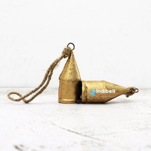 May include: Two gold-colored metal bell ornaments with a cone shape and a rope for hanging. One bell is upright, and the other is lying on its side. The bells have a rustic, textured finish.