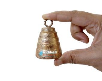 May include: A small, gold-colored bell with a tiered design and a loop at the top. The bell is being held by a hand.