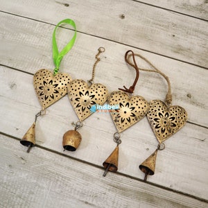 A set of four heart metal cutouts with vintage designs, each attached to bells and hung with various ribbons and strings.
