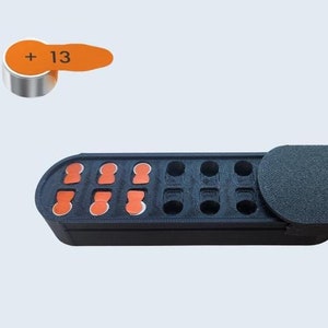 May include: A black plastic storage case with a hinged lid. The case has 12 compartments, each with a small orange circle inside. The case is designed to hold small batteries. The label on the battery reads " + 13"