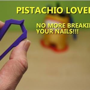 May include: A purple pistachio opener held in a hand. The opener is a small, U-shaped tool with a rectangular opening. Text in the image reads "PISTACHIO LOVERS" and "NO MORE BREAKING YOUR NAILS!!!"