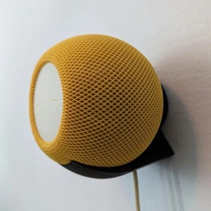 May include: A yellow smart speaker with a black wall mount. The speaker has a mesh grille and a white front panel.
