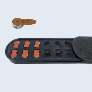 May include: A black plastic case with a hinged lid, containing 10 small, round, orange-brown battery cells. The case is labeled with the text "312" and a plus sign. A single battery cell is shown separately.