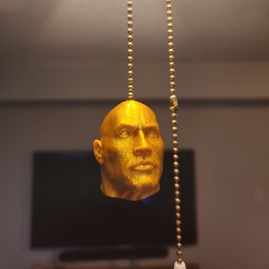 Könnte beinhalten: Ein goldfarbener 3D-gedruckter Kopf eines Mannes, der an einer goldenen Kette hängt. Der Kopf ist detailliert und realistisch, mit einem ernsten Ausdruck.