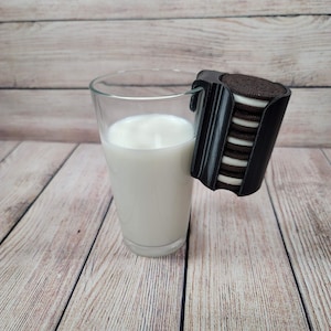 Könnte beinhalten: Ein Glas Milch mit einem schwarz-weißen Kekshalter, der an der Seite befestigt ist. Der Kekshalter ist mit Schokoladen-Sandwich-Keksen gefüllt.