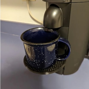 May include: A blue speckled mug with a black handle sits on a black mug holder attached to a Nespresso coffee machine.