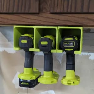 May include: Three green and black cordless drills are mounted on a wall-mounted holder. The holder has three compartments, each with a label that says "ONE+ HP 18V BRUSHLESS".