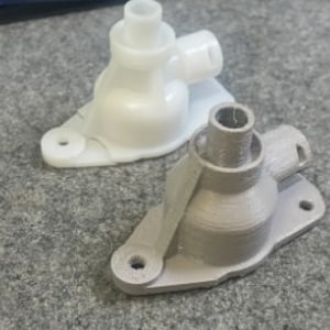 Könnte beinhalten: Zwei 3D-gedruckte Kunststoffverbinder, einer weiß und einer grau, mit mehreren Öffnungen und einer flachen Basis.