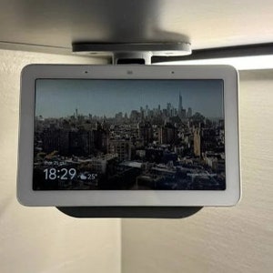 Peut inclure: Un écran intelligent blanc avec une ville en arrière-plan sur l'écran. L'heure est 18h29 et la température est de 25 degrés. L'écran est monté au plafond.