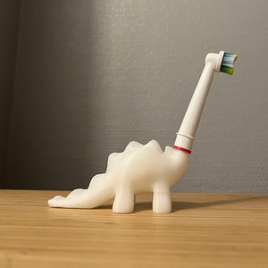May include: White plastic dinosaur toothbrush holder with a white electric toothbrush head attached to the top.