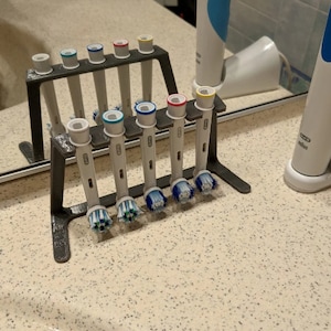 May include: A gray plastic stand with eight slots for holding electric toothbrush heads. The stand is holding seven toothbrush heads with different colored bristles. The toothbrush heads are in a row, with the bristles facing forward.