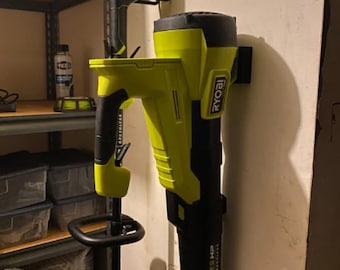 Può includere: Un soffiatore per foglie Ryobi nero e verde e un decespugliatore Ryobi nero e verde sono montati su una parete bianca con supporti a parete neri. Il soffiatore per foglie ha la scritta "ONE+ HP" stampata sul lato.