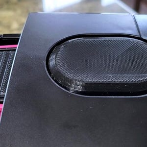 May include: Close-up of a black coffee maker with a removable water reservoir and a filter holder. The coffee maker has a textured, oval-shaped button on the top.