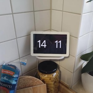 Peut inclure: Une horloge numérique blanche affichant l'heure 14:11, montée sur un mur en carrelage blanc. L'horloge est placée dans un coin de la pièce.