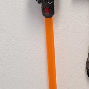 Puede incluir: Una aspiradora inalámbrica con una varilla naranja brillante, un cuerpo gris oscuro y una parte superior y un cabezal de cepillo azules. La aspiradora está montada en una pared, mostrando su diseño elegante y su estética moderna. El diseño de la aspiradora incluye un cabezal de cepillo en forma de flor.