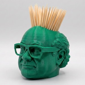 May include: A green 3D-printed head-shaped toothpick holder with a full head of toothpicks. The head is wearing green-rimmed glasses. The holder is a novelty item, perfect for a kitchen or dining room.