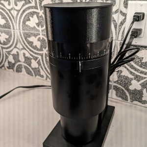 May include: A black electric coffee grinder with a timer dial that goes from 5 to 10 seconds. The grinder has a black base and a black hopper. The grinder is plugged in and ready to use.