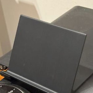 Puede incluir: Un soporte negro en ángulo para sostener una tableta o un teléfono. El soporte está hecho de un material resistente y tiene un diseño elegante y moderno.