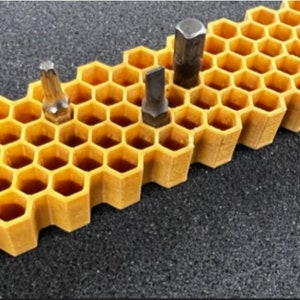 May include: A yellow honeycomb-shaped organizer with multiple slots for holding small tools, such as screwdriver bits.  Five screwdriver bits are visible in the slots.