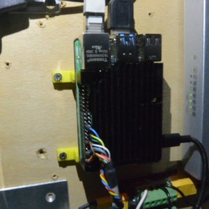 May include: A black Raspberry Pi computer with a green circuit board and a black heatsink is mounted to a wooden surface with yellow plastic brackets. The computer is connected to a white ethernet cable, a black USB cable, and a variety of other wires.