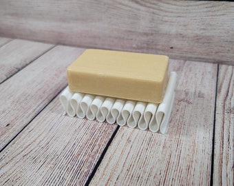 May include: A white soap dish with a wavy design holds a rectangular bar of light brown soap.
