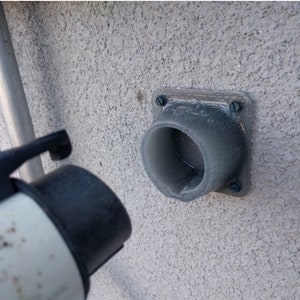 May include: A grey plastic electrical outlet cover with a round opening, mounted on a textured wall. A black and white electrical cord is plugged into the outlet.