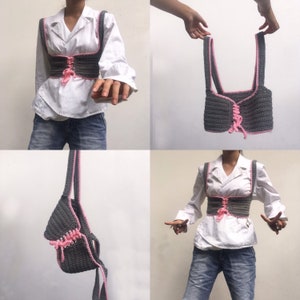 K&ouml;nnte beinhalten: Ein graues H&auml;keltop mit rosa Besatz und einer Schn&uuml;rung vorne. Das Top wird an einem Modell gezeigt und an einem Haken aufgeh&auml;ngt.
